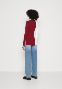 Maglione a coste in bordeaux e bianco, design aderente con spacchi laterali, abbinato a jeans a gamba larga azzurri a vita alta e stivali neri.
