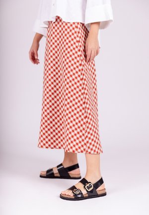 Sandalias negras con acentos de doble hebilla, plantilla de corcho, combinadas con una falda de cuadros roja y blanca, de longitud a mitad de pantorrilla, corte relajado.