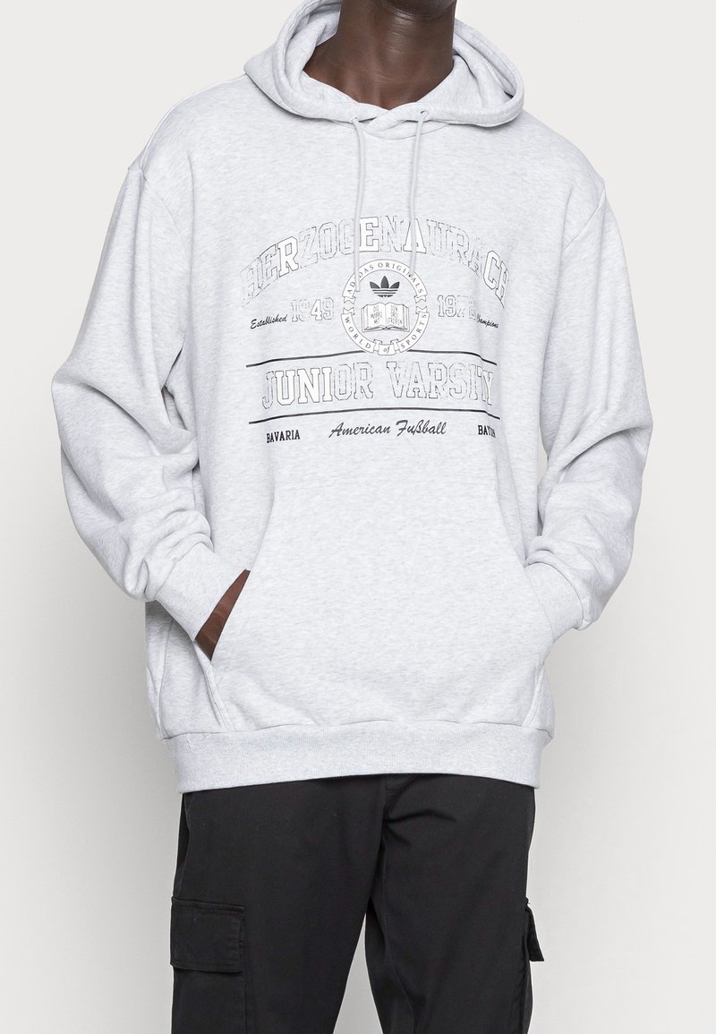 Grå hoodie med dragsko i huvan, frampocket och tryckt text. Har ribbade ärmslut och fåll, tillverkad av mjukt bomullsblandat material.