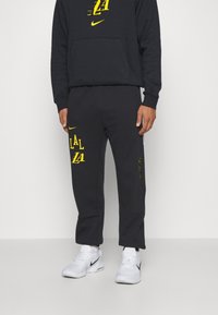 Sort Nike hoodie med gul "LA" logo, parret med matchende sorte træningsbukser med gule accenter og lynlåslommer. Hvide sneakers.