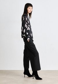 Zwarte bloemenblouse met witte en roze accenten, gecombineerd met zwarte wijde broekspijpen en zwarte enkelboots met puntige neus en scriptdetail.
