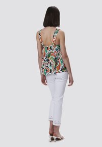 Kleurvolle patroonloze mouwloze top met een lage rug, gecombineerd met witte broek met een decoratieve oogletafwerking aan de zoom.