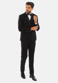 Completo smoking nero con giacca doppiopetto, rever in satin e scarpe nere eleganti. Camicia bianca con papillon nero; vestibilità su misura, tessuto liscio.