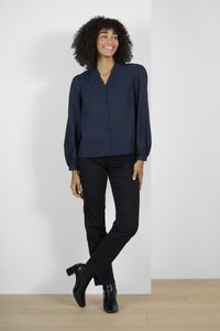 Blouse bleu marine à boutons avec un col texturé et de longues manches bouffantes, assortie à un pantalon noir et des bottines à talons noires.