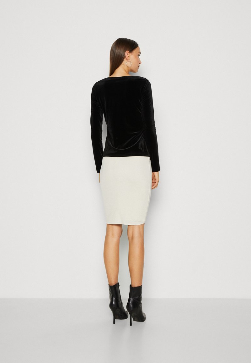 Schwarzes Samtoberteil mit langen Ärmeln, kombiniert mit einem hellbeigen Bleistiftrock, getragen mit schwarzen Stiefeletten, die eine glatte Textur und einen maßgeschneiderten Sitz zeigen.