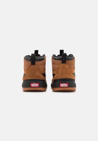 Brązowe zamszowe sneakersy wysokie z czarnymi akcentami, z teksturowanym tyłem, wyściełanym kołnierzem i gumową podeszwą, z widoczną etykietą z logo.