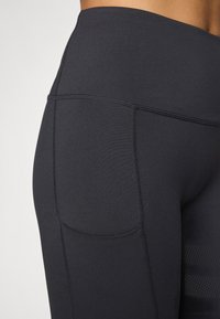 Schwarze High-Waist-Leggings aus dehnbarem Material, mit einer Seitentasche, flachen Nähten und einer glatten, matten Textur.