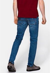 Modré džíny v úzkém střihu, s moderátní praním a jemným vyblednutím. Zadní kapsy mají prošívaný design. Nosené se šedými botami.