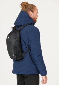 Black backpack with mesh accents, worn over a blue insulated jacket. Features adjustable straps and a zippered main compartment.
