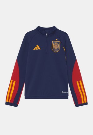 Marineblauwe sportpullover met rode mouwen, gele strepen en een voorrits. Kenmerkt het embleem van het Spaanse nationale team en het Adidas-logo.