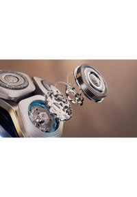 Electric razor with metallic finishing, circular heads, intricate blade design, and blue accents. Components are depicted in an exploded view.