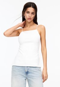 Top bianco senza maniche con scollo quadrato e spalline sottili, realizzato in un tessuto liscio e leggero, abbinato a jeans in denim chiari.
