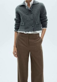 Cardigan grise raccourci avec des boutons double boutonnage, manches retroussées et tricot texturé. Associé à un pantalon à carreaux marron taille haute.