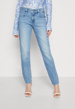Light blue denim jeans with a straight-leg cut, featuring five pockets and a zip fly. Paired with white heeled sandals.