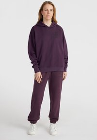 Felpa viola con cappuccio e pantaloni della tuta abbinati realizzati in morbido cotone, caratterizzati da una vestibilità rilassata e polsini elasticizzati; testo rilevante stampato in nero.