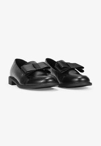 Black leather loafers with a rounded toe, featuring a large black fabric bow on each shoe and a low, flat rubber sole. Smooth texture.