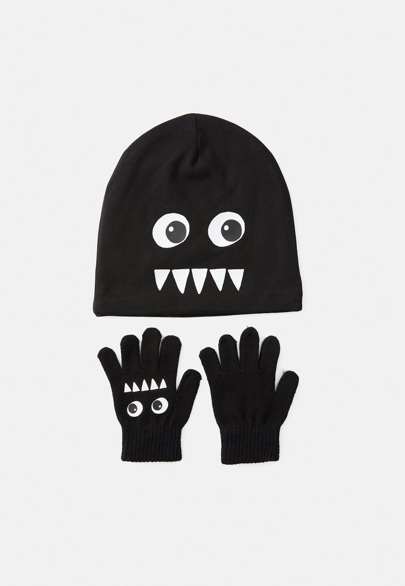 Zwarte beanie met een witte monster-gezichtsgrafiek, met grote ogen en tanden, gecombineerd met bijpassende zwarte handschoenen met soortgelijke ontwerpelementen.
