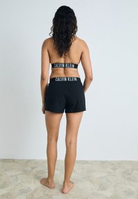 Soutien-gorge de sport noir Calvin Klein assorti à un short, fabriqué dans un tissu doux, avec une taille élastique portant le logo et une coupe décontractée.