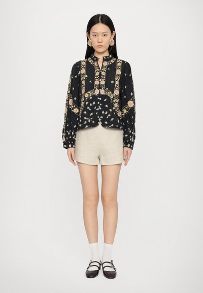 Blusa nera a fantasia floreale con maniche lunghe e colletto abbottonato abbinata a pantaloni corti color crema. Accompagnata da grandi orecchini e scarpe con cinturino.