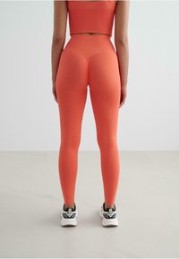 Leggings a vita alta, aderenti, di un vivace corallo, realizzati in materiale elasticizzato. Abbinati a scarpe sportive bianche e nere.