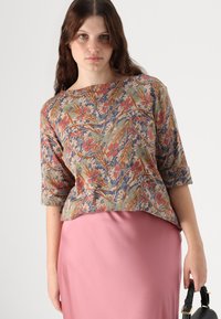 Haut à motif floral dans des couleurs atténuées avec des manches trois-quarts, associé à une jupe rose unie. Tissu léger, silhouette simple.