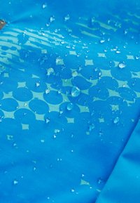 Tissu imperméable bleu avec une texture lisse, présentant des gouttes d'eau à la surface. Les motifs notables incluent des formes circulaires et en étoile.