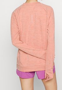 Lättviktig, långärmad träningsskjorta i mjuk korall med melerat mönster, med en reflexdetalj längs ryggen och raglanärmar.