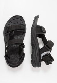 Black sandals with adjustable straps, rubber soles, and a textured interior. Features durable materials and a sporty design.