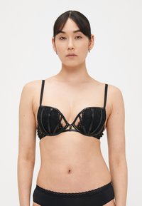 Reggiseno nero con coppe in pizzo, dettagli lucidi, supporto con ferretto e spalline regolabili. Include dettaglio decorativo traforato e fascia elastica.