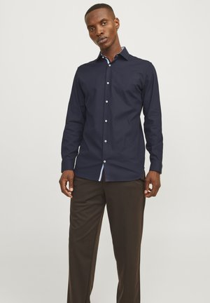 Chemise à manches longues bleu marine avec un col boutonné, présentant des boutons blancs et des accents bleu clair au niveau du col et de l'ourlet, confectionnée dans un tissu lisse.