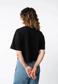 Zwarte, gekropte t-shirt van zacht materiaal met korte mouwen en een ronde halslijn. Gekleed met lichtblauwe hoge taille jeans.