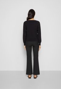 Svart tröja med texturerade, öppet stickade ärmar, kombinerad med svarta utsvängda byxor. Outfiten har en avslappnad passform och en minimalistisk design.