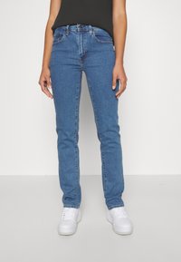 Jeans skinny blu in denim con cinque tasche, chiusura con bottone e cerniera, leggermente elasticizzati; abbinati a sneakers bianche.