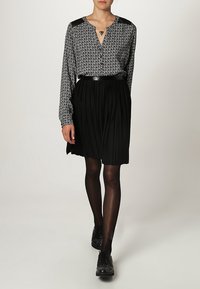 Jupe plissée noire associée à une chemise à boutons à motifs avec des accents noirs sur les épaules. Complétée par des collants noirs et des chaussures noires à clous.