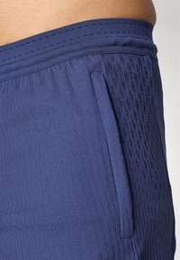 Mørkeblå treningsshorts med et teksturert mønster og sidelomme. Livsnæringen har en glatt, elastisk finish med små perforeringer.