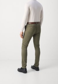 Pantalon vert olive à coupe slim avec poches arrière ; une ceinture marron et des chaussures noires complètent la tenue. Tissu doux avec une texture lisse.