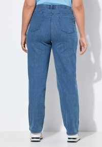 Jeans de denim azul claro con cinturilla elástica, corte recto, dos bolsillos traseros y una sutil textura vertical. Combinados con zapatillas blancas.