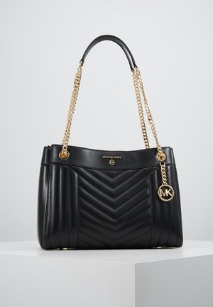 Black leather Michael Kors handbag with chevron quilting, gold chain straps, and round gold MK logo charm on a white surface.