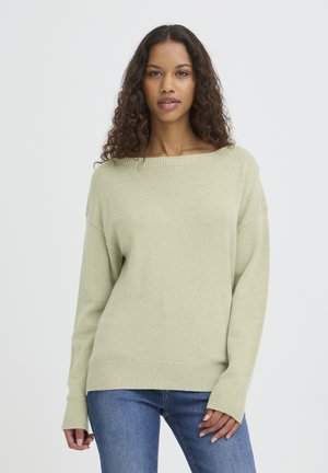 Hellgrüner Pullover aus weichem Strickmaterial mit weitem Ausschnitt, gerippten Bündchen und langen Ärmeln, kombiniert mit blauen Jeans.