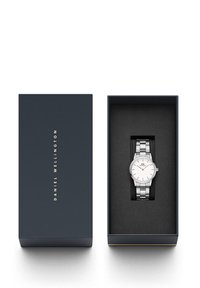 Silver wristwatch with a white dial and metal bracelet, presented in a navy blue box with gold lettering on the lid. Black interior.