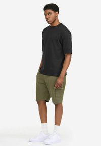 Black short-sleeve t-shirt paired with olive green cargo shorts. Model wears white sneakers and crew-length white socks, minimalist design.