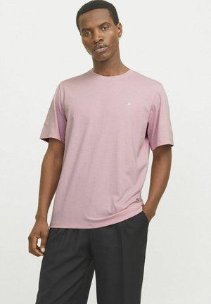 Kortærmet, rundhalset t-shirt i blødt lyserødt stof, med et lille logo på brystet, parret med løse sorte bukser.