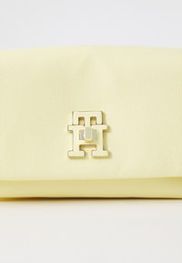 Pochette en simili cuir jaune avec une texture lisse et un accent logo doré brillant à l'avant. Design plié sans embellissements supplémentaires.