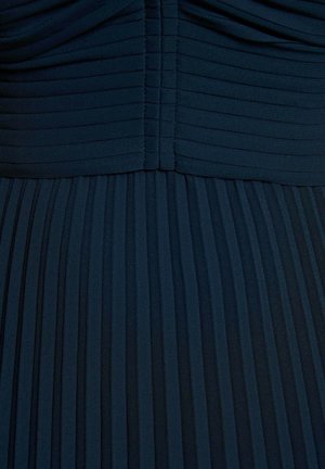 Mørkeblå plissert stof, der går fra vandrette folder øverst til lodrette plisseringer nedenfor, hvilket fremhæver tekstur og syningsdetaljer.