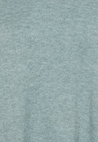 Helles blaues gestricktes Gewebe mit einer weichen, strukturierten Oberfläche, das ein feines, gleichmäßiges Gewebe und subtile Farbschattierungen zeigt. Es sind keine Muster oder Hardware sichtbar.