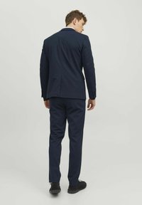 Abito blu navy con design su misura, apertura singola e pantaloni coordinati. Vestibilità slim con una texture liscia. Scarpe nere completano l'outfit.