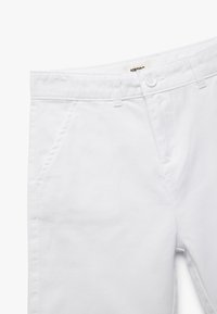 Pantaloni bianchi in cotone con una texture liscia, dotati di tasche anteriori, chiusura con bottone e passanti per la cintura. Design semplice senza motivi.