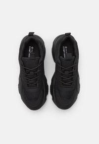 Chaussures de sport noires en matériaux synthétiques avec dessus en mesh, semelles épaisses, fermeture à lacets et boucles de traction sur la languette.