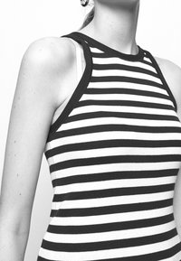 Svart och vit randig ärmlös topp med ribbat mönster, försedda med en rund halsringning och kontrasterande mörk kant runt ärmarna.