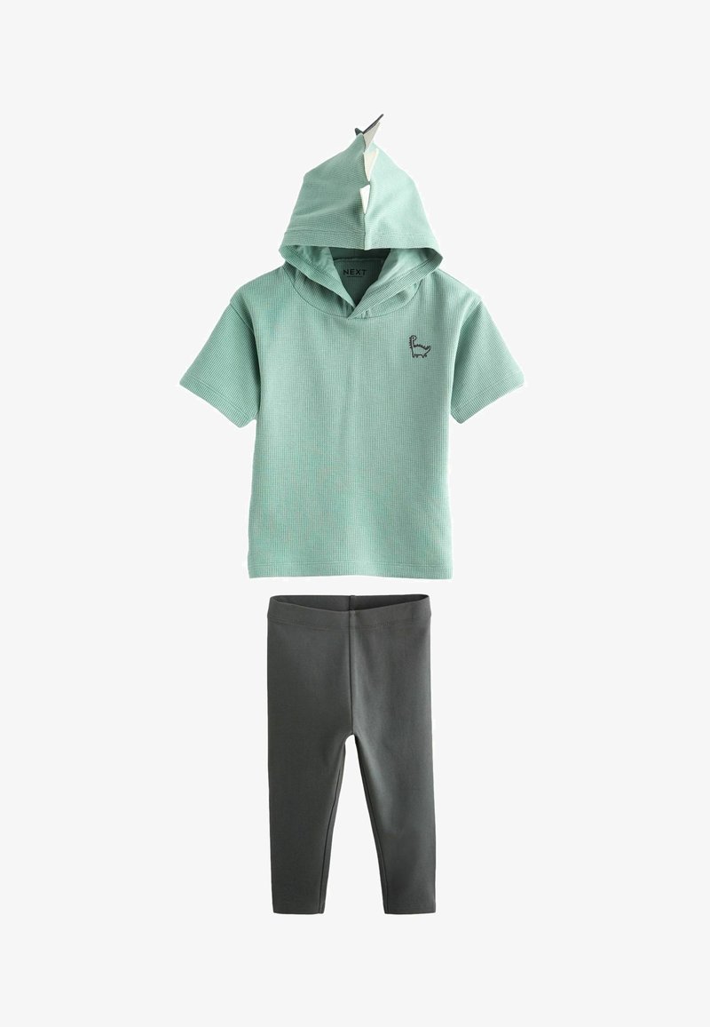 Miętowa koszula z krótkim rękawem i kapturem, z emblematem lamy, zestawiona z czarnymi legginsami. Materiał w mieszance bawełny o prążkowanej fakturze.